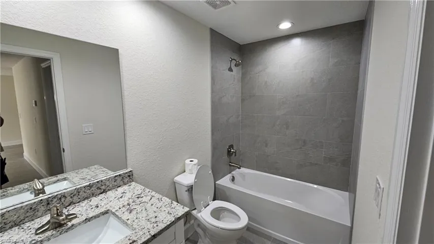 Full bath featuring toilet, shower / tub combination, vanity, and a textured wall