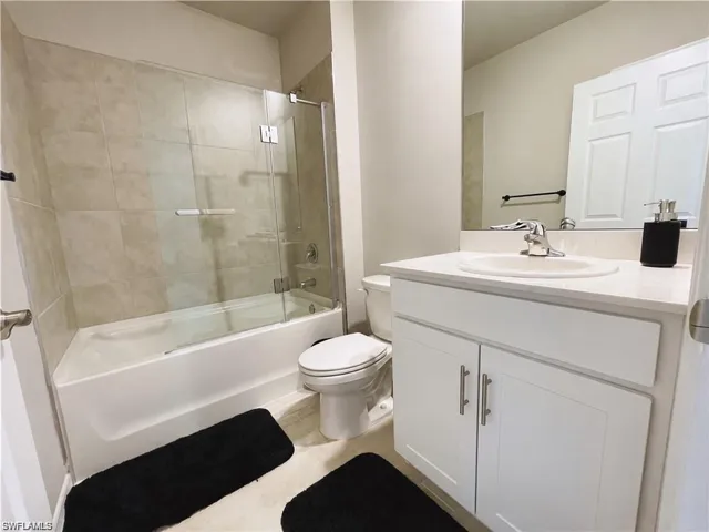 Bathroom featuring a white vanity cabinet with a stone countertop, an integrated sink with a chrome faucet, a large wall-mounted mirror, and a tub-shower combination with floor-to-ceiling tile surrounds and a glass panel door
