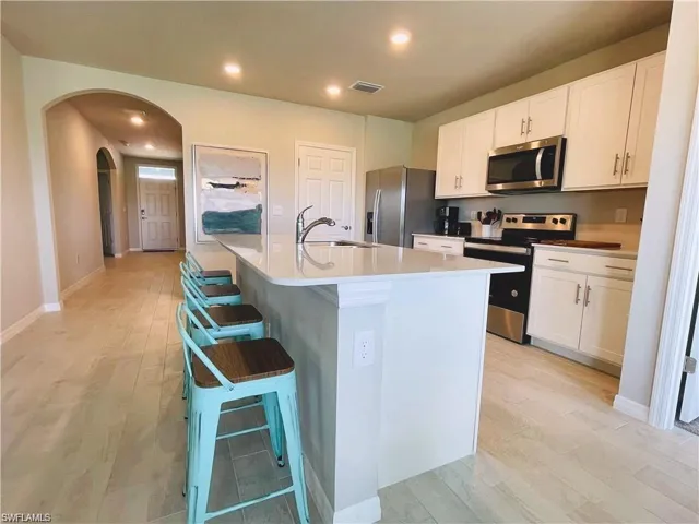 Kitchen featuring white shaker-style cabinetry, quartz countertops, a central island with a stainless steel sink, stainless steel appliances, and wood-finish flooring