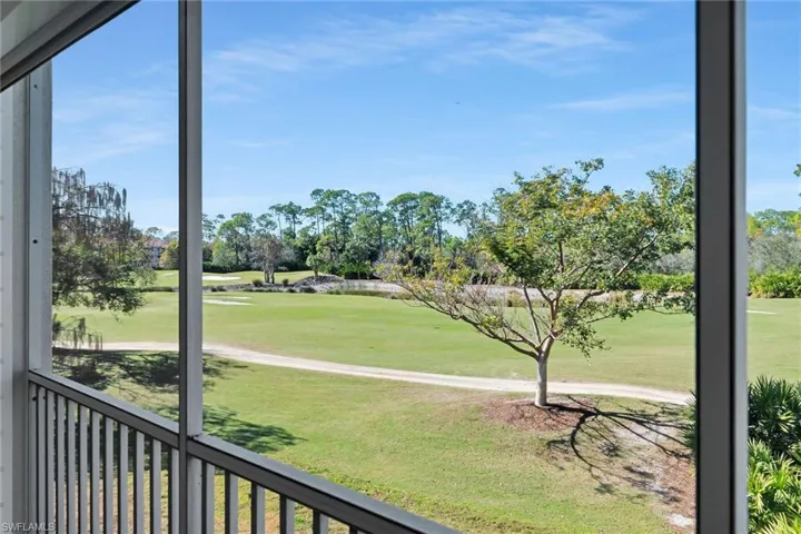 View of green lawn featuring view of golf course and a sunroom