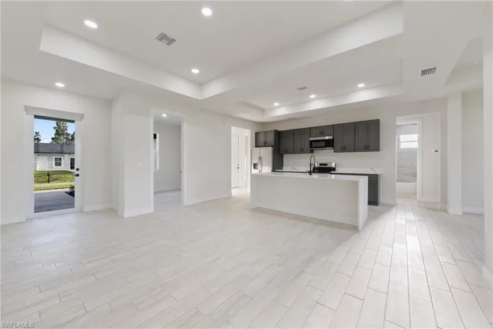 Kitchen featuring open floor plan, an island with sink, a tray ceiling, wood tiled floors, and stainless steel appliances