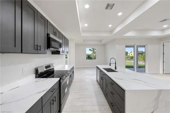 Kitchen with stainless steel appliances, light stone counters, recessed lighting, a large island, and a tray ceiling