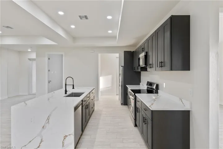 Kitchen with stainless steel appliances, light stone counters, recessed lighting, a kitchen island with sink, and light wood-type flooring