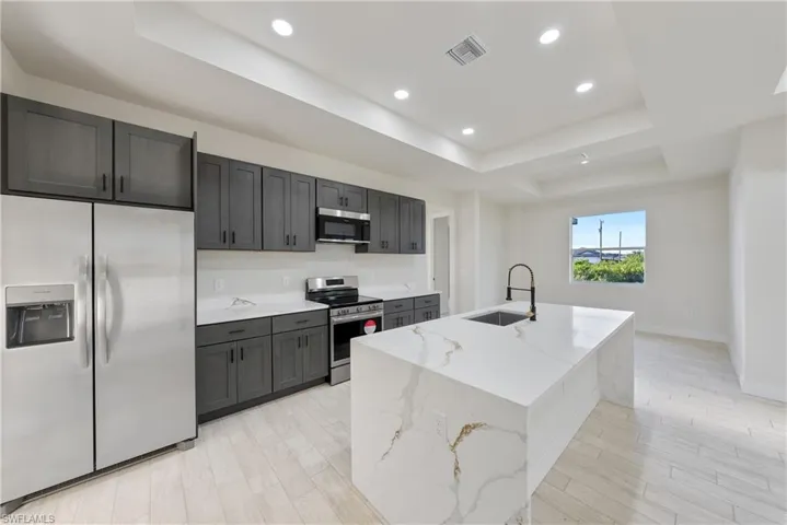 Kitchen with stainless steel appliances, a tray ceiling, recessed lighting, light stone counters, and light wood finished floors