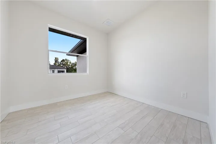 Spare room featuring light wood-style flooring and vaulted ceiling
