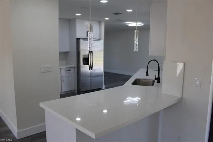 Kitchen featuring white cabinetry, kitchen peninsula, stainless steel fridge with ice dispenser, and decorative light fixtures