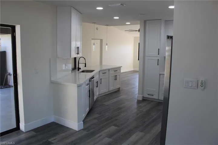Kitchen with dark wood-type flooring, white cabinets, sink, stainless steel dishwasher, and ceiling fan