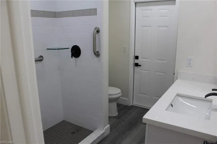 Bathroom featuring tiled shower, hardwood / wood-style floors, vanity, and toilet