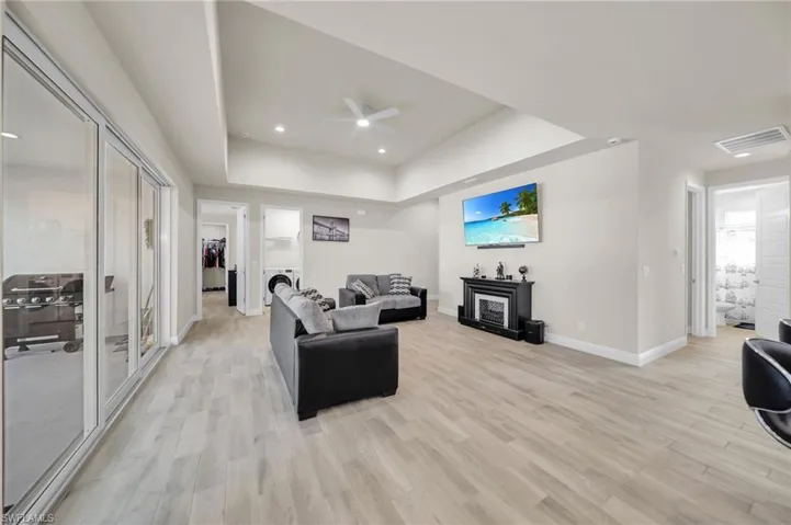 Living room featuring washer / clothes dryer, ceiling fan, a raised ceiling, baseboards, and light wood-type flooring