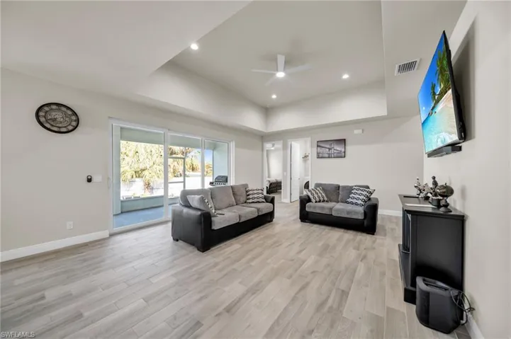Living room featuring visible vents, ceiling fan, light wood-style flooring, and a raised ceiling