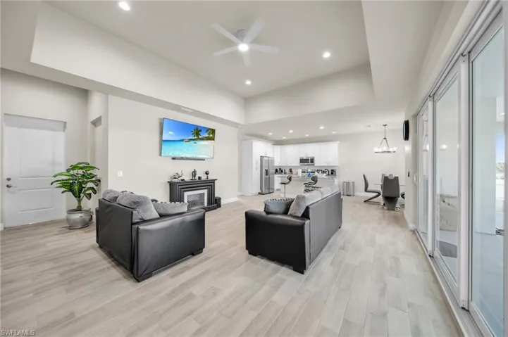 Living area with recessed lighting, ceiling fan with notable chandelier, light wood-style flooring, and a glass covered fireplace