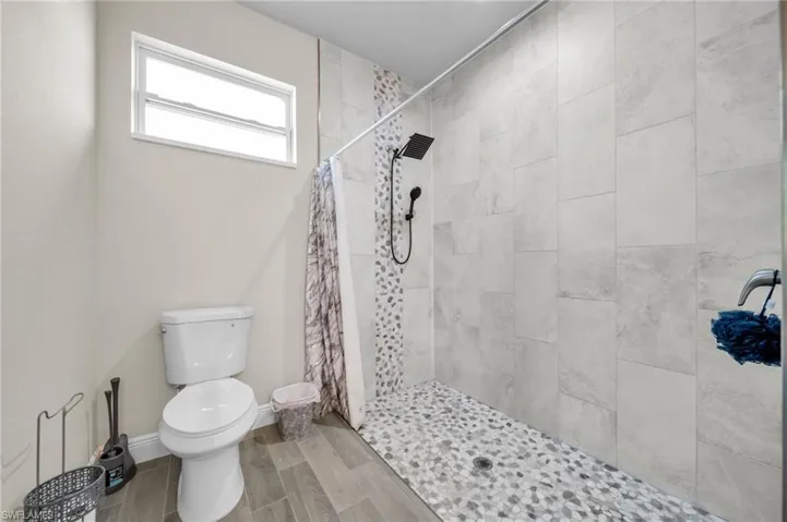 Full bath featuring toilet, tiled shower, and wood finished floors