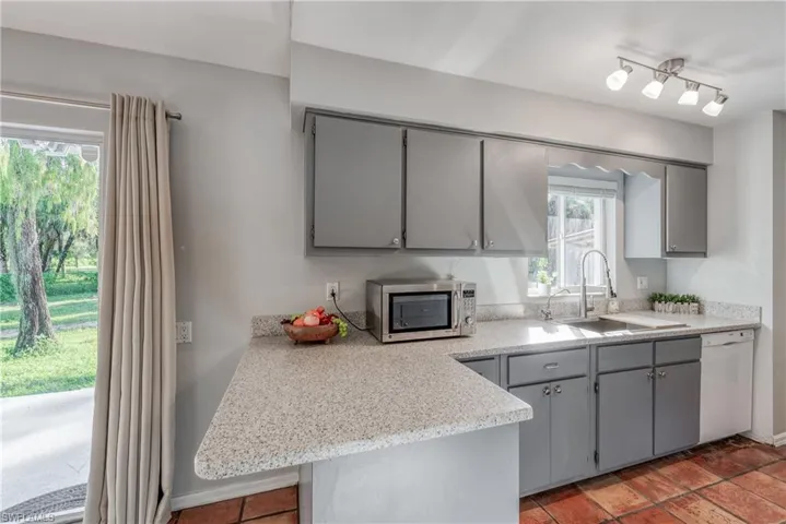 Kitchen with dishwasher, light stone counters, kitchen peninsula, sink, and gray cabinetry