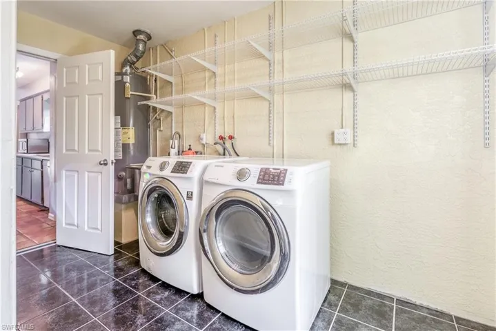 Laundry room featuring gas water heater, separate washer and dryer, and dark tile patterned flooring