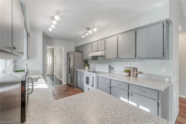 Kitchen with gray cabinets, appliances with stainless steel finishes, and light stone countertops