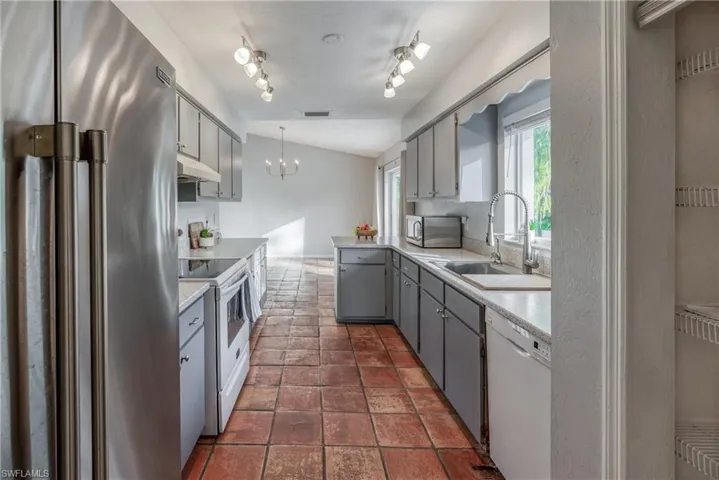Kitchen featuring vaulted ceiling, decorative light fixtures, stainless steel appliances, sink, and rail lighting