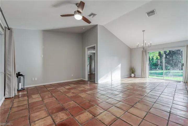 Spare room featuring lofted ceiling, ceiling fan with notable chandelier, and tile patterned floors