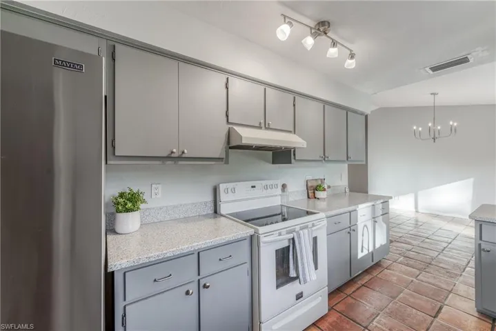 Kitchen featuring gray cabinetry, lofted ceiling, stainless steel refrigerator, and electric stove