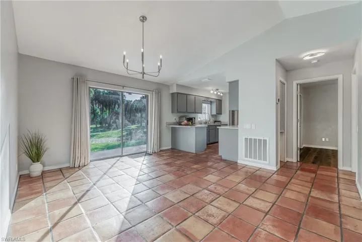 Unfurnished living room with light tile patterned floors, vaulted ceiling, a notable chandelier, and sink