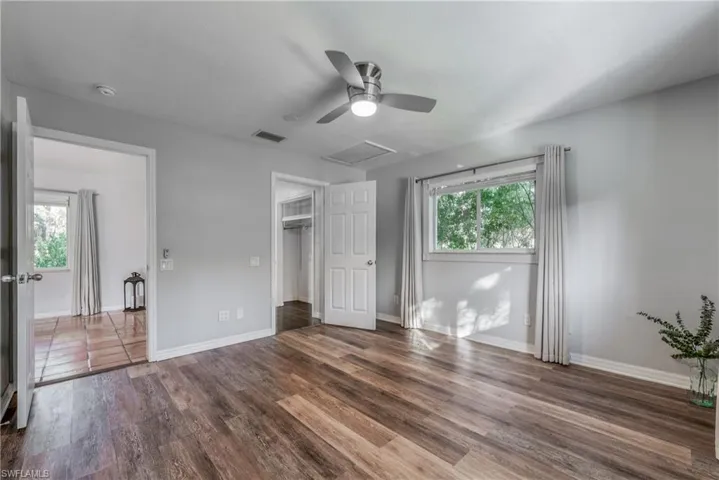 Unfurnished bedroom with ceiling fan, a walk in closet, multiple windows, and dark hardwood / wood-style flooring
