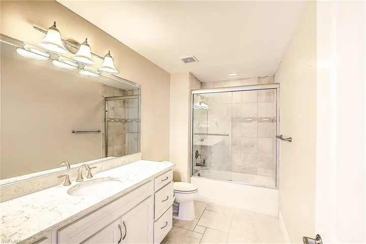 Full bathroom featuring vanity, toilet, tile patterned flooring, and bath / shower combo with glass door