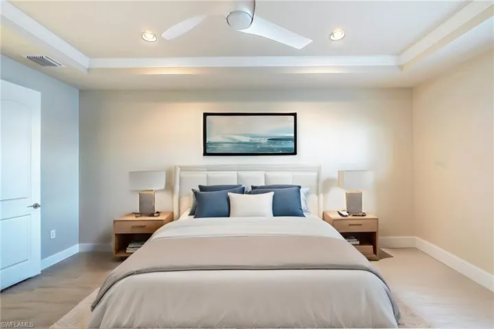 Bedroom featuring ceiling fan, ornamental molding, light wood-type flooring, and a tray ceiling