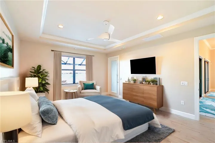 Bedroom with a tray ceiling, ornamental molding, ceiling fan, and light hardwood / wood-style floors
