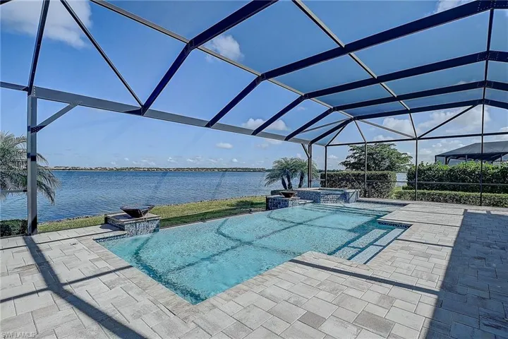 View of swimming pool with a lanai, a water view, an in ground hot tub, pool water feature, and a patio