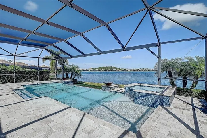 View of swimming pool with a lanai, a water view, a patio area, and an in ground hot tub