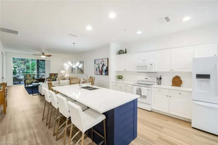 Two tone kitchen with white appliances, suspended lighting, a kitchen island with sink, a breakfast bar, and light wood-style flooring