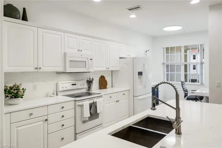Kitchen featuring white appliances, white cabinetry, light stone countertops, and recessed lighting