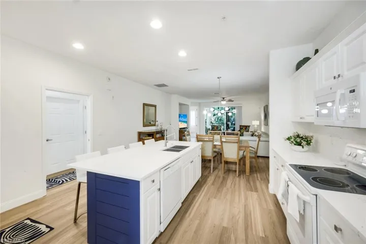 Kitchen with white appliances, a breakfast bar, white cabinets, a kitchen island with sink, and light wood-style floors