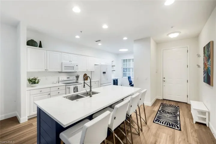 Kitchen featuring white cabinets, a kitchen breakfast bar, white appliances, an island with sink, and light wood-style floors