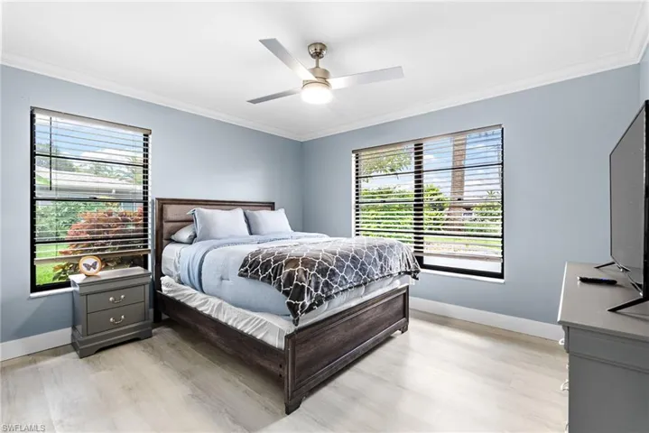 Bedroom with ornamental molding, multiple windows, light wood finished floors, and a ceiling fan