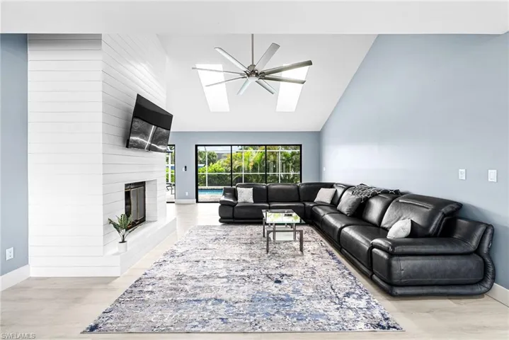 Living room with high vaulted ceiling, a large fireplace, light wood finished floors, a skylight, and a ceiling fan