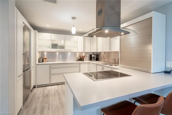 Kitchen with black electric cooktop, light wood-type flooring, backsplash, pendant lighting, and island range hood