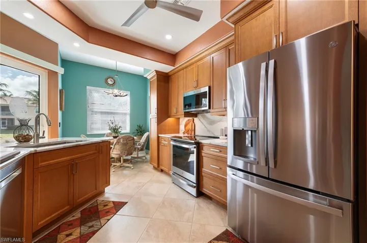 Kitchen with stainless steel appliances, light tile patterned flooring, ceiling fan, light stone counters, and wood finish cabinets