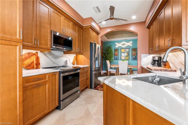 Kitchen featuring wood finish cabinets, stainless steel appliances, light stone counters, decorative backsplash, and recessed lighting