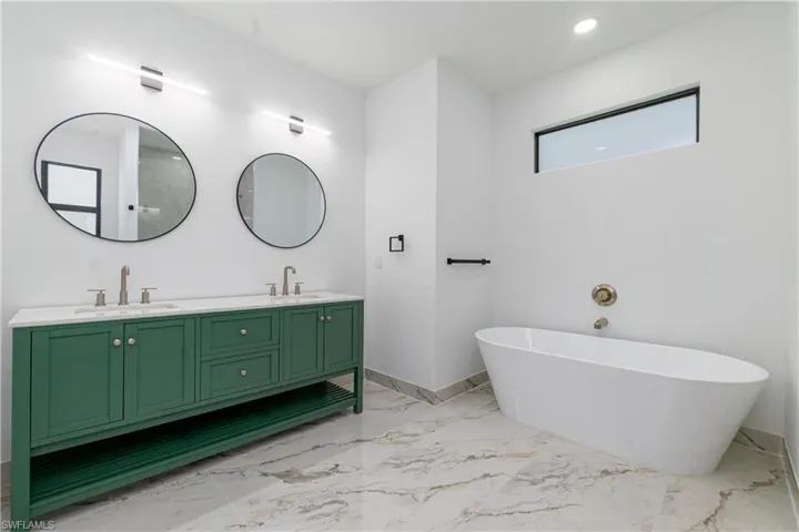 Full bathroom with double vanity, a soaking tub, marble finish floors, and recessed lighting