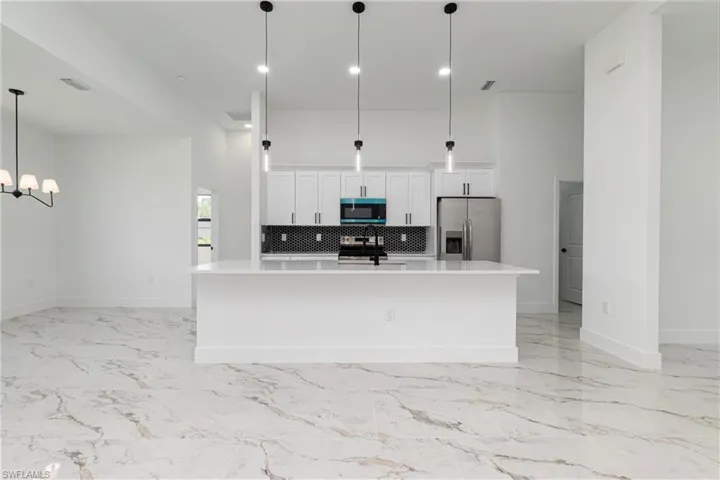 Kitchen featuring appliances with stainless steel finishes, light countertops, white cabinets, a spacious island, and backsplash