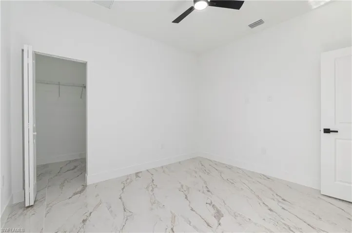 Unfurnished bedroom with marble finish flooring, a spacious closet, and ceiling fan
