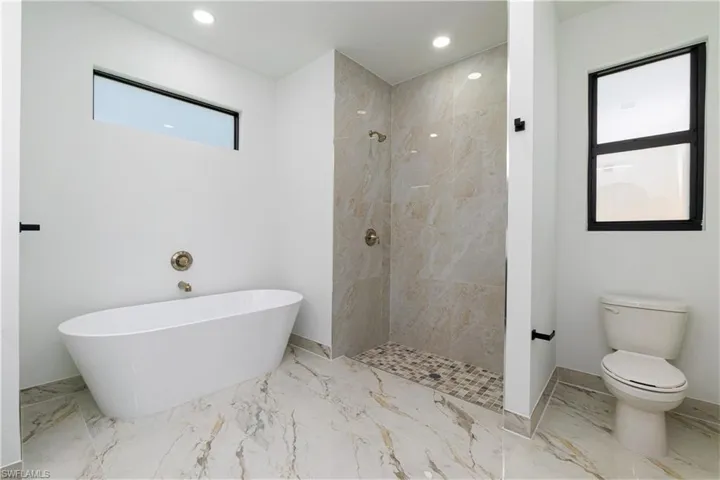 Bathroom featuring a freestanding bath, tiled shower, marble finish flooring, and recessed lighting