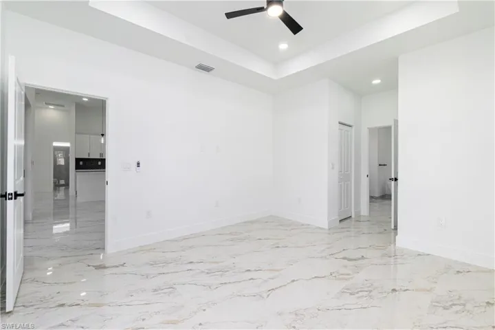 Empty room with a raised ceiling, recessed lighting, light marble finish flooring, and ceiling fan