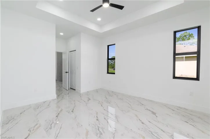 Spare room with a tray ceiling, recessed lighting, marble finish floors, and ceiling fan