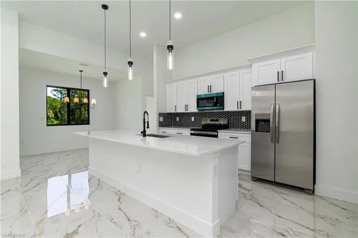 Kitchen featuring stainless steel appliances, white cabinets, backsplash, a center island with sink, and recessed lighting