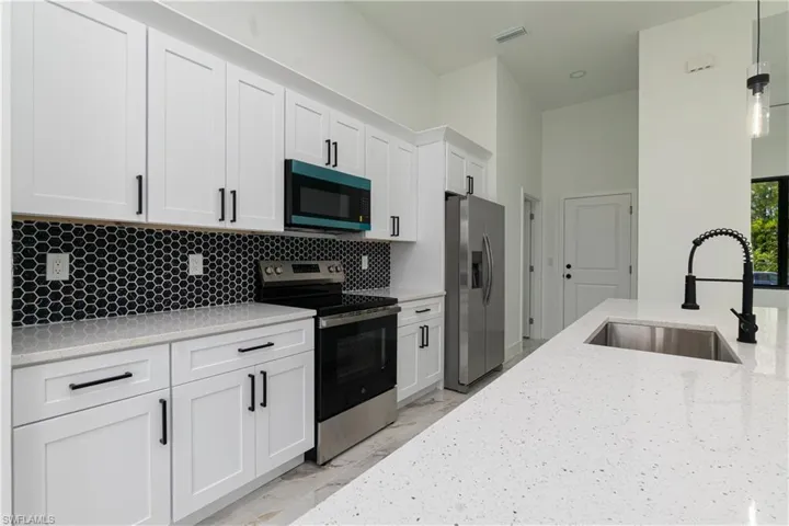 Kitchen featuring stainless steel appliances, white cabinetry, hanging light fixtures, light stone countertops, and tasteful backsplash