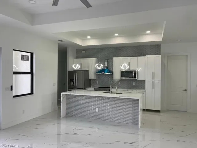 Kitchen featuring a tray ceiling, appliances with stainless steel finishes, light stone counters, and white cabinetry