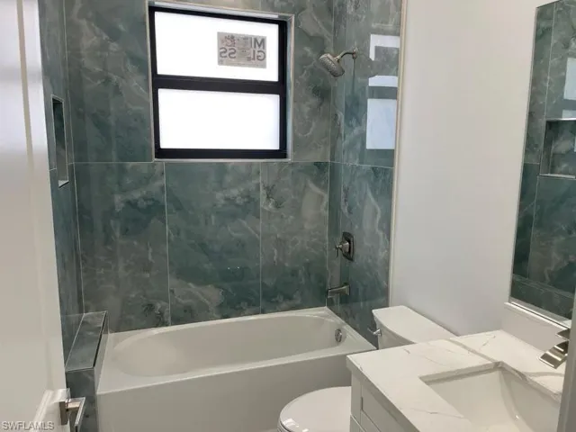 Full bathroom with tiled shower / bath combo, vanity, and toilet