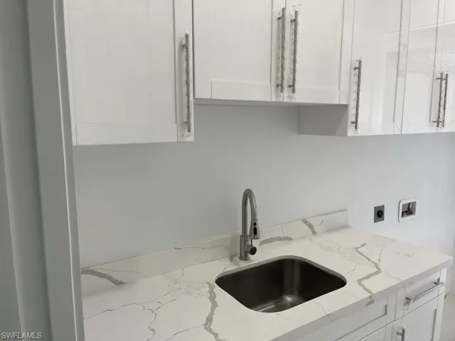 Kitchen with light stone counters, white cabinets, and sink