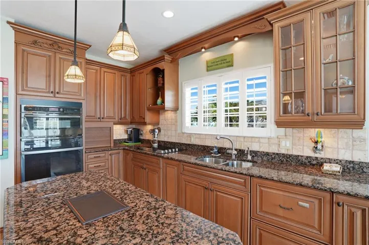 Kitchen featuring dark stone countertops, wood finish cabinets, double oven, decorative light fixtures, and glass insert cabinets